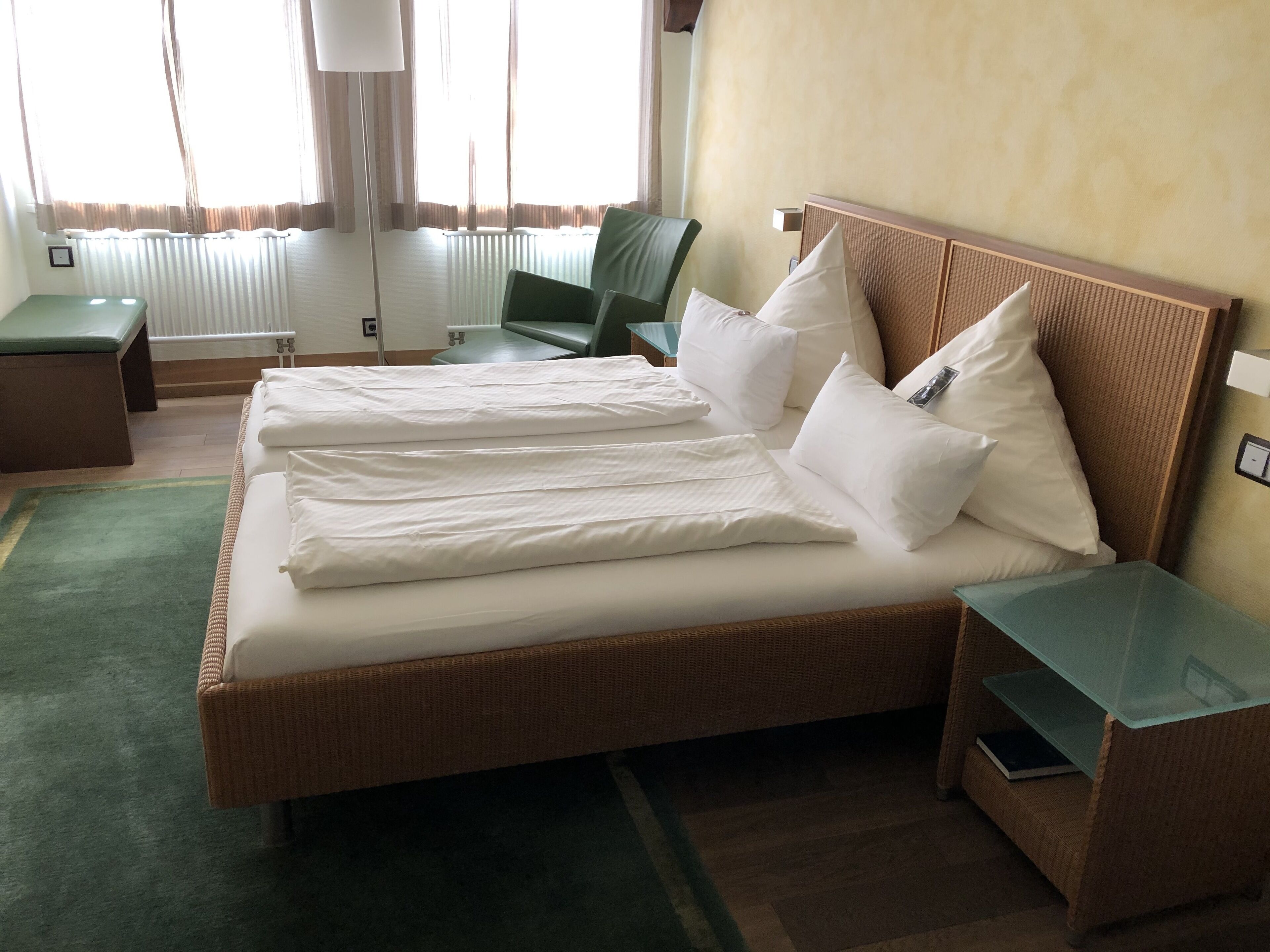Habitación de hotel con una cama grande, dos mesitas de noche, una silla verde y una lámpara.