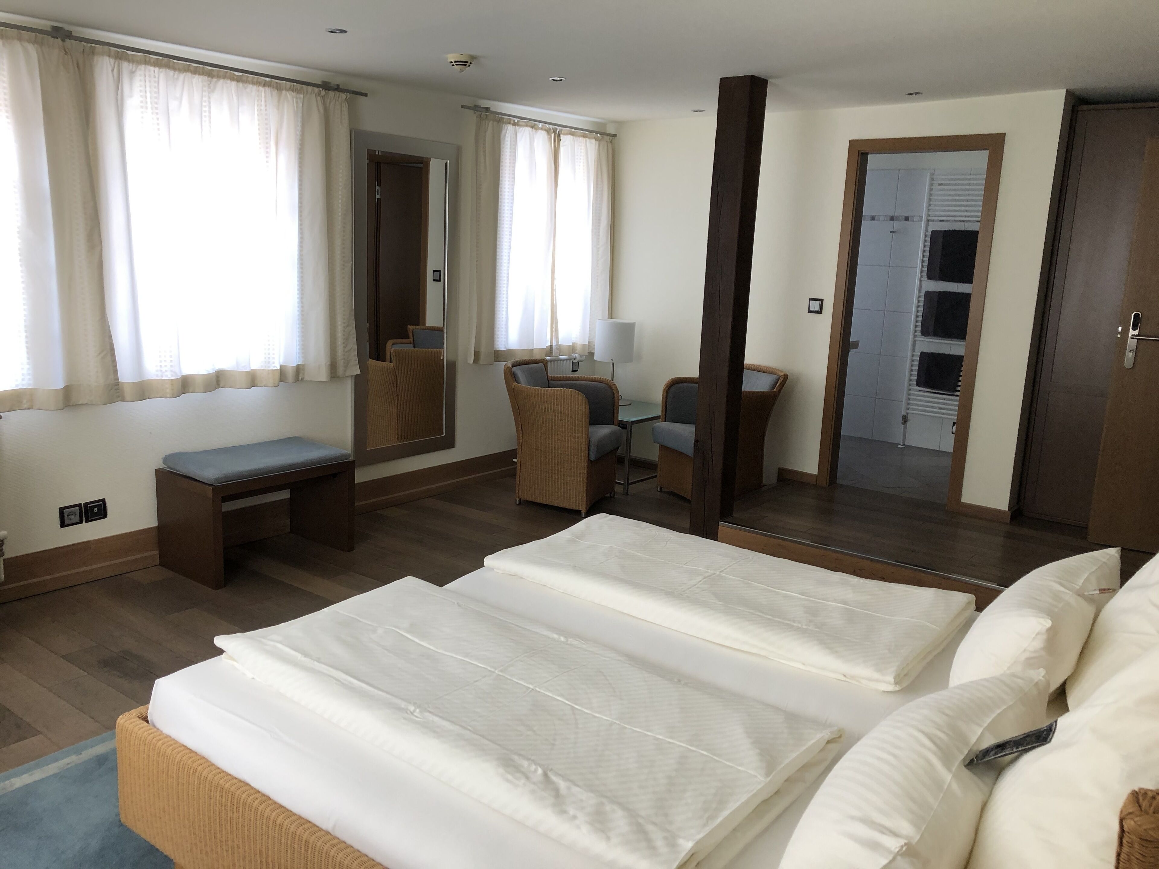 Une chambre d’hôtel avec deux lits, un bureau, une chaise, un miroir et une porte donnant sur une salle de bain.