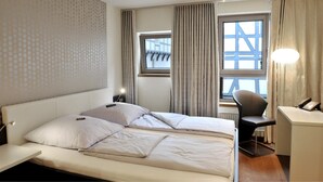 A hotel room with a bed, a desk, a chair, a lamp, and a window with curtains. - CENTRINUM Altstadt-Hotel (Melsungen)