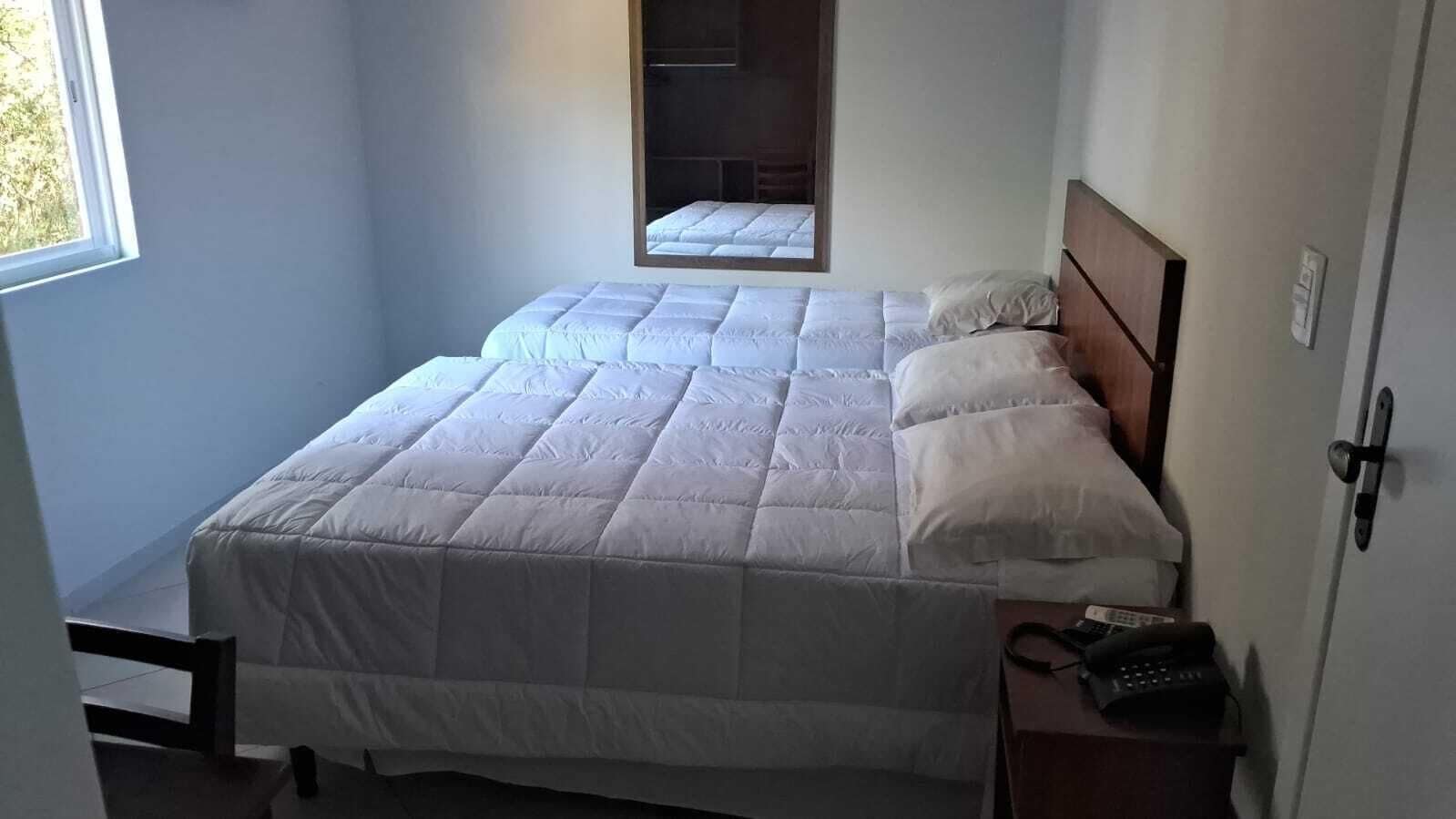 Una cama individual con cabecera, una mesita de noche con teléfono y una ventana que da a vistas de vegetación.