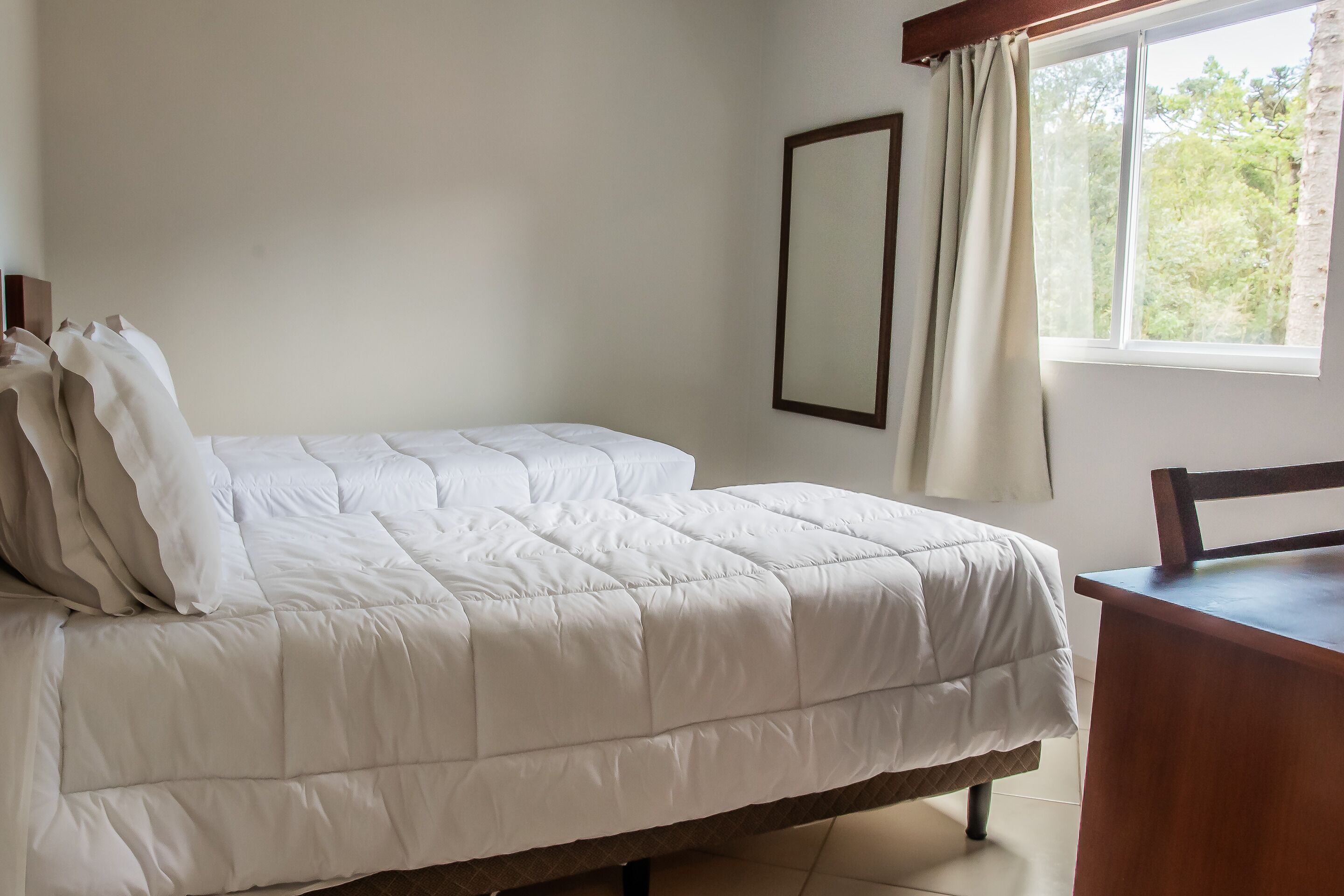 A single bed with a white duvet in a room with a window and a wooden desk.