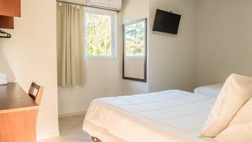A bedroom with a bed, a desk, a chair, a TV, and a window with curtains.