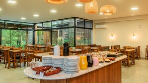 Ein gut beleuchteter Speiseraum mit Holztischen und -stühlen, einer Buffettheke mit verschiedenen Speisen und großen Fenstern mit Blick auf Grünflächen.