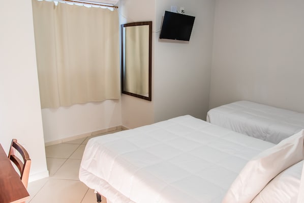 Quarto com duas camas, um espelho, uma televisão e uma janela com cortinas.