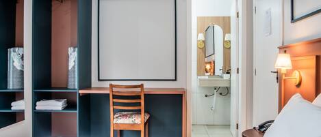 Une chambre d’hôtel comprenant un lit, un bureau, une chaise, une armoire, un miroir et une table de chevet avec une lampe.
