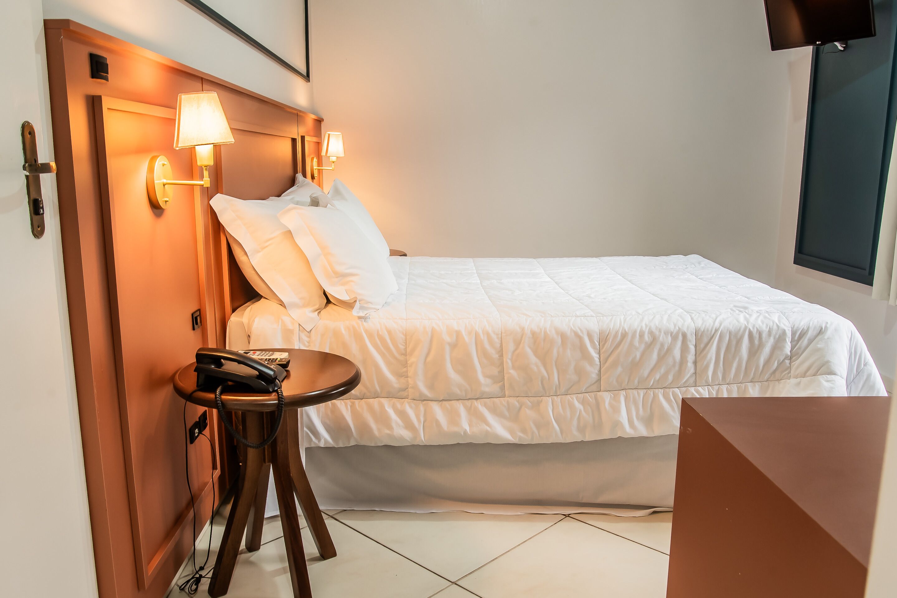 A hotel room with a bed, bedside lamps, a telephone, and a small table.