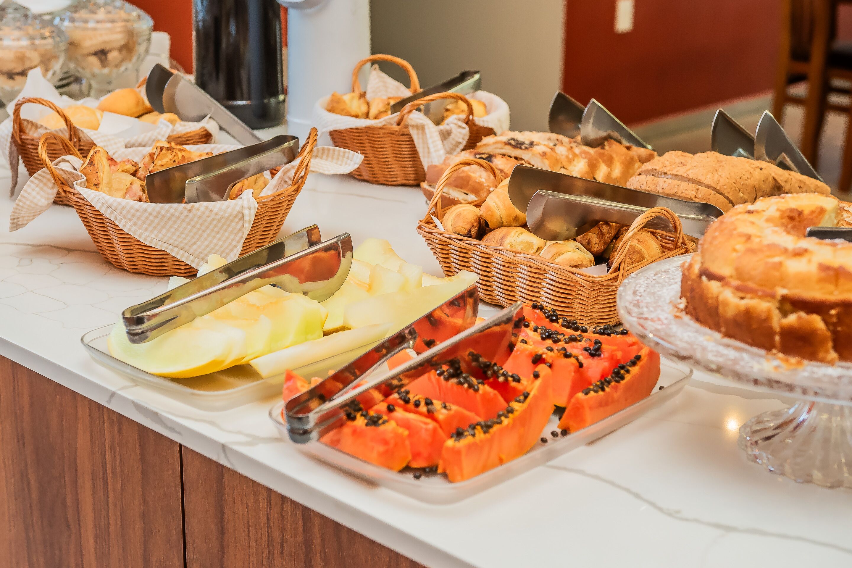 Una mesa de buffet con panes, pasteles y frutas cortadas.