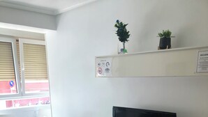 A living room with a flat-screen TV on a white cabinet, a floral sofa, a dining table with chairs, and a balcony with a view. - Apartment near the Sardinero (Santander)