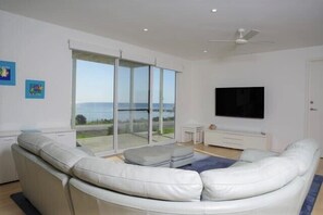 Relax in this stylish living room with a sofa, flat-screen TV, and sliding glass door leading to a balcony with a sea view.