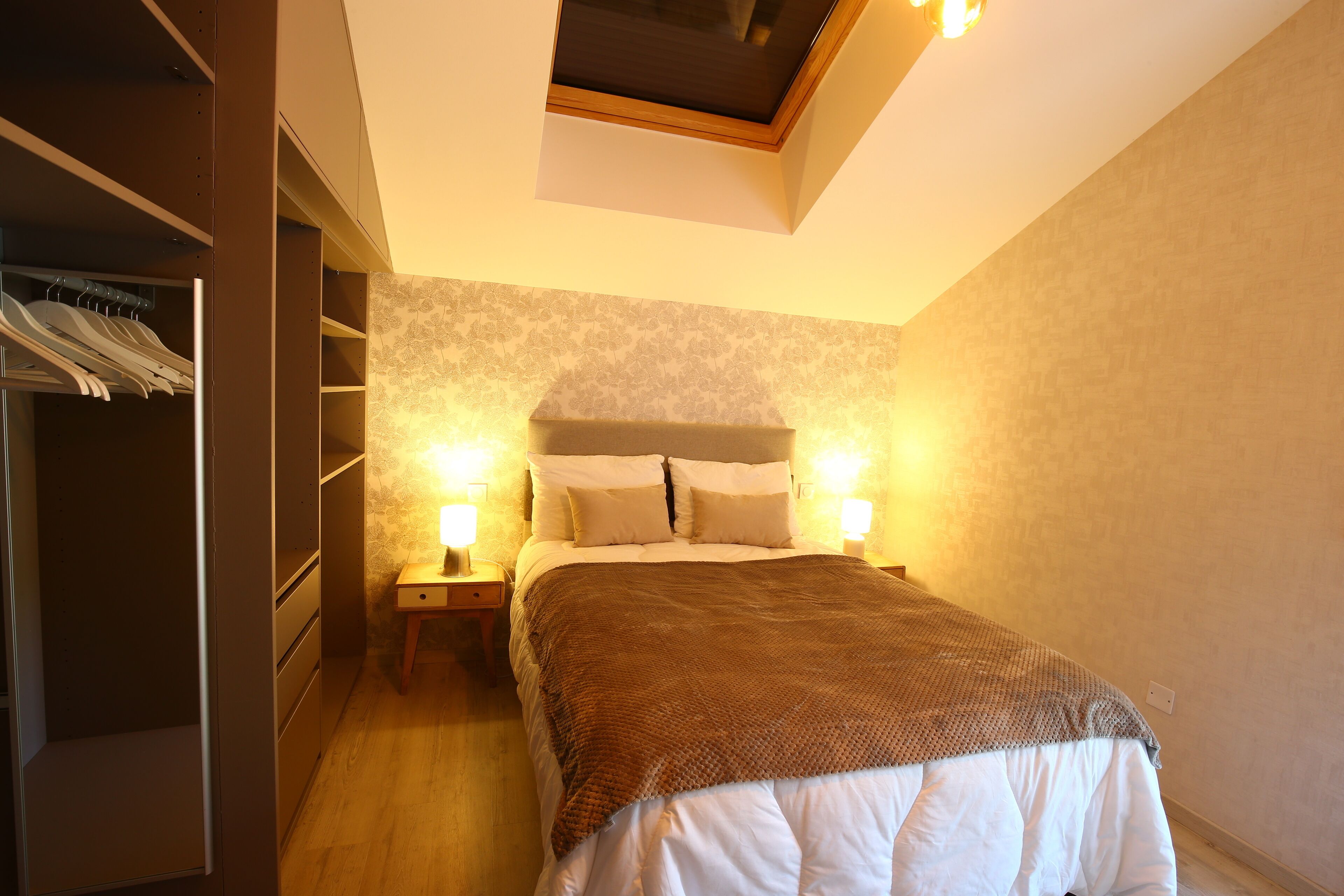 A bedroom with a bed, nightstands, a wardrobe, and a skylight.