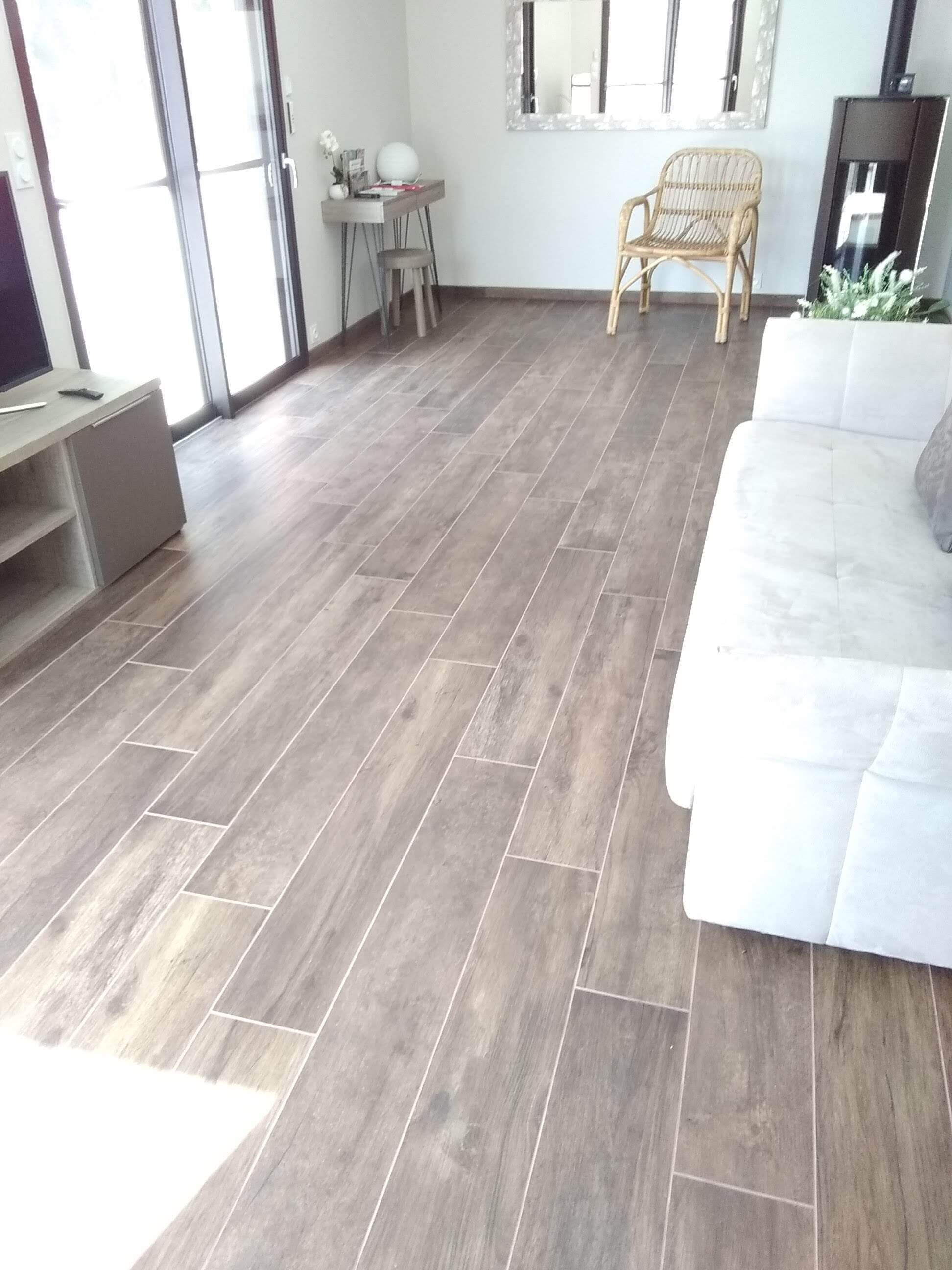 Uma sala de estar moderna com piso de azulejos cinza, um sofá branco, uma poltrona de vime e uma pequena mesa com objetos decorativos.
