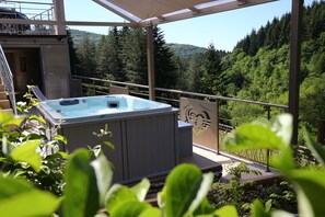 Un jacuzzi en un balcón con vistas a una ladera boscosa.