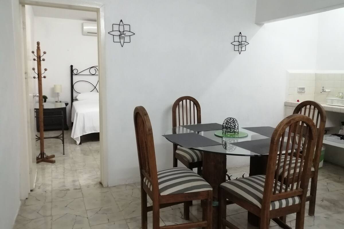 Un coin repas comprenant une table en verre, quatre chaises en bois avec des coussins à rayures et deux appliques murales.