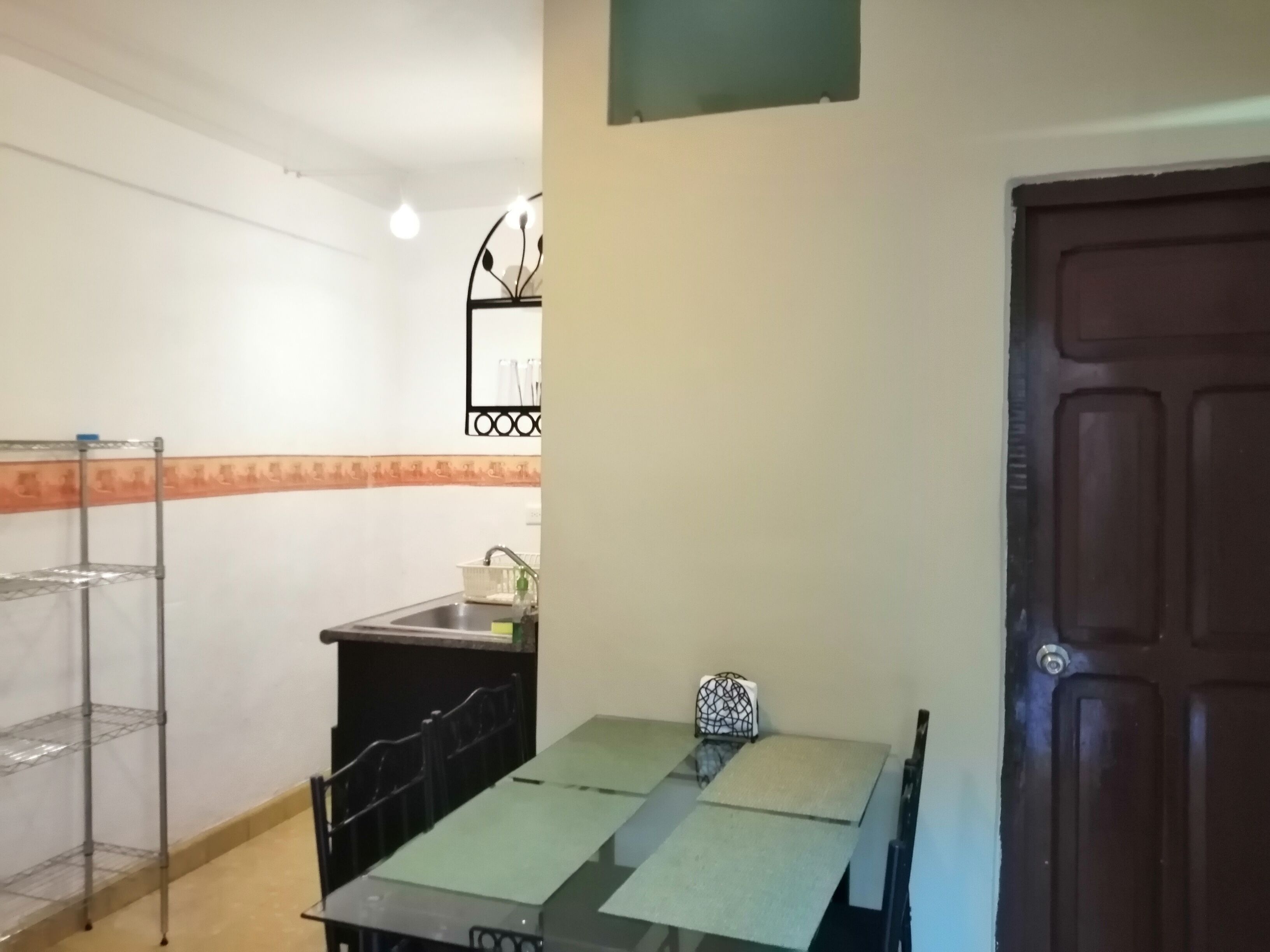 A small kitchen with a sink, a metal shelf, and a table.