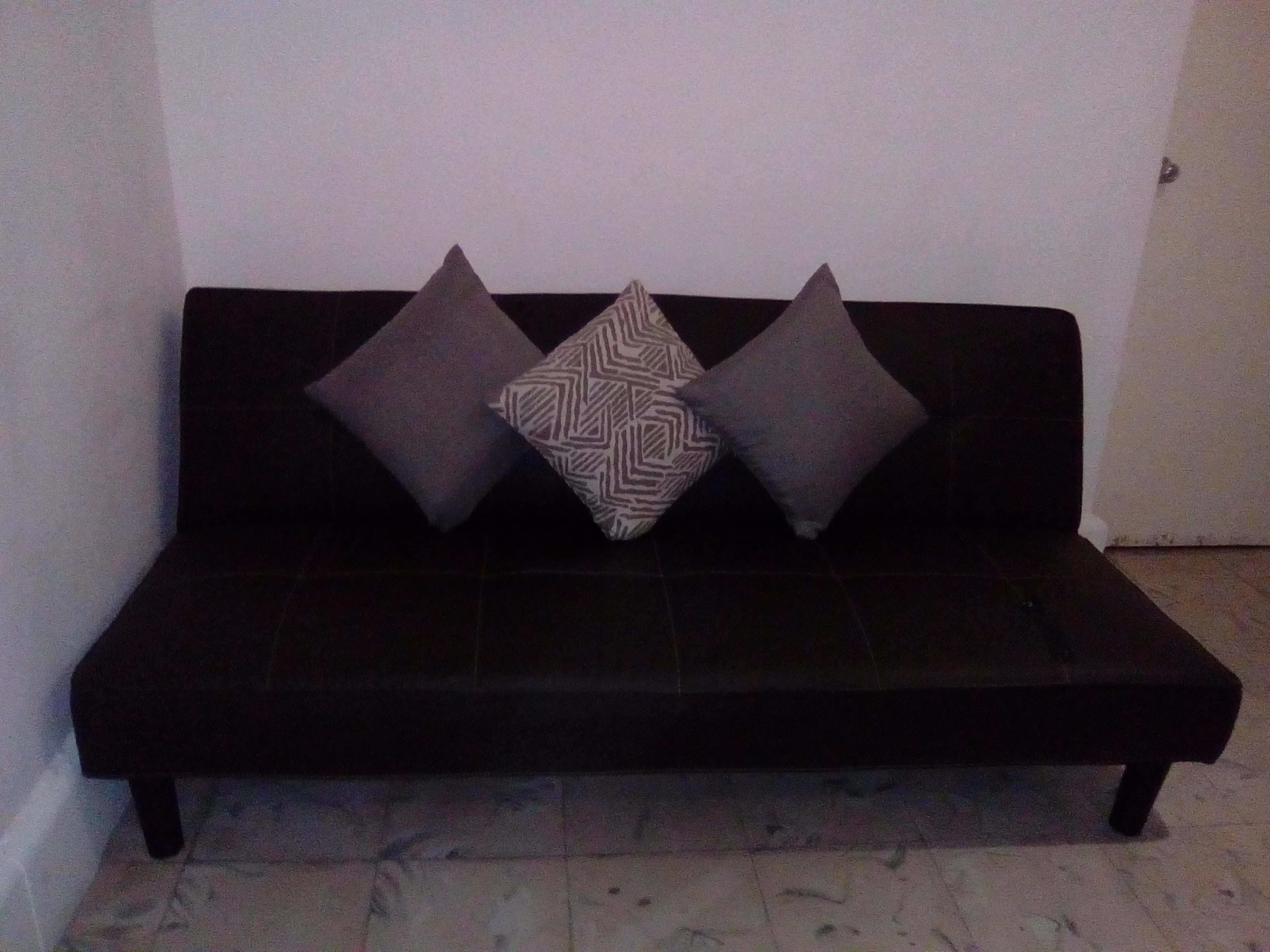A black sofa with three patterned cushions against a plain wall.