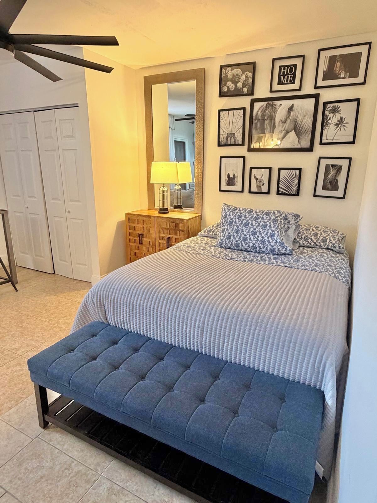 A bedroom with a bed, a bench, a mirror, and framed pictures on the wall.