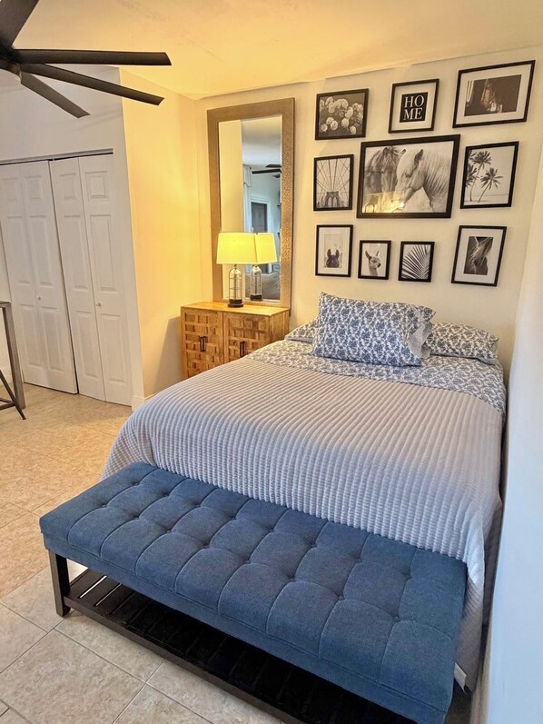 A bedroom with a bed, a bench, a mirror, and framed pictures on the wall.