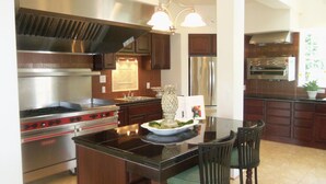 A modern kitchen with a central island, stainless steel appliances, wooden cabinets, and a chandelier.