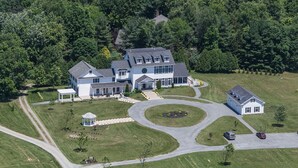 A large, two-story house with a circular driveway, surrounded by well-maintained lawns and trees.
