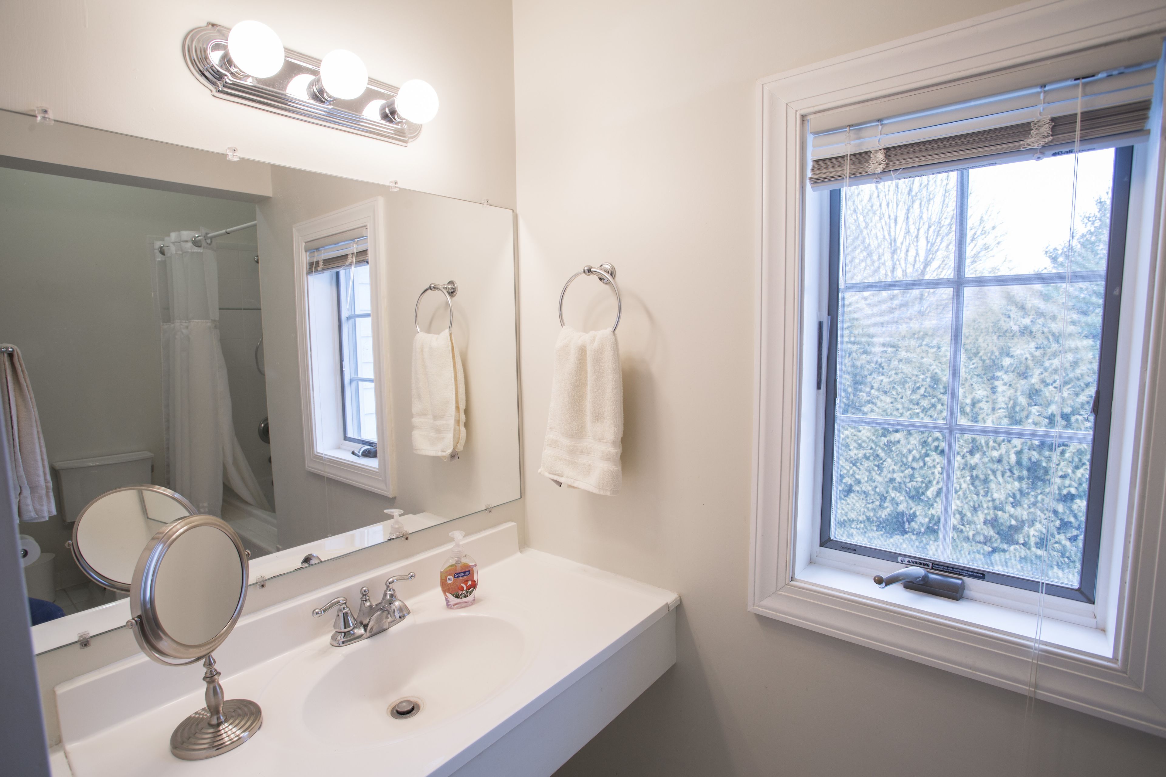 A bathroom with a white sink, mirror, and vanity, a window with frosted glass, and a shower curtain.