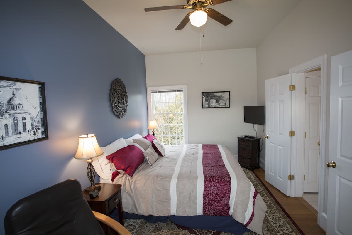 A bedroom with a bed, a desk, a chair, a ceiling fan, and a door.