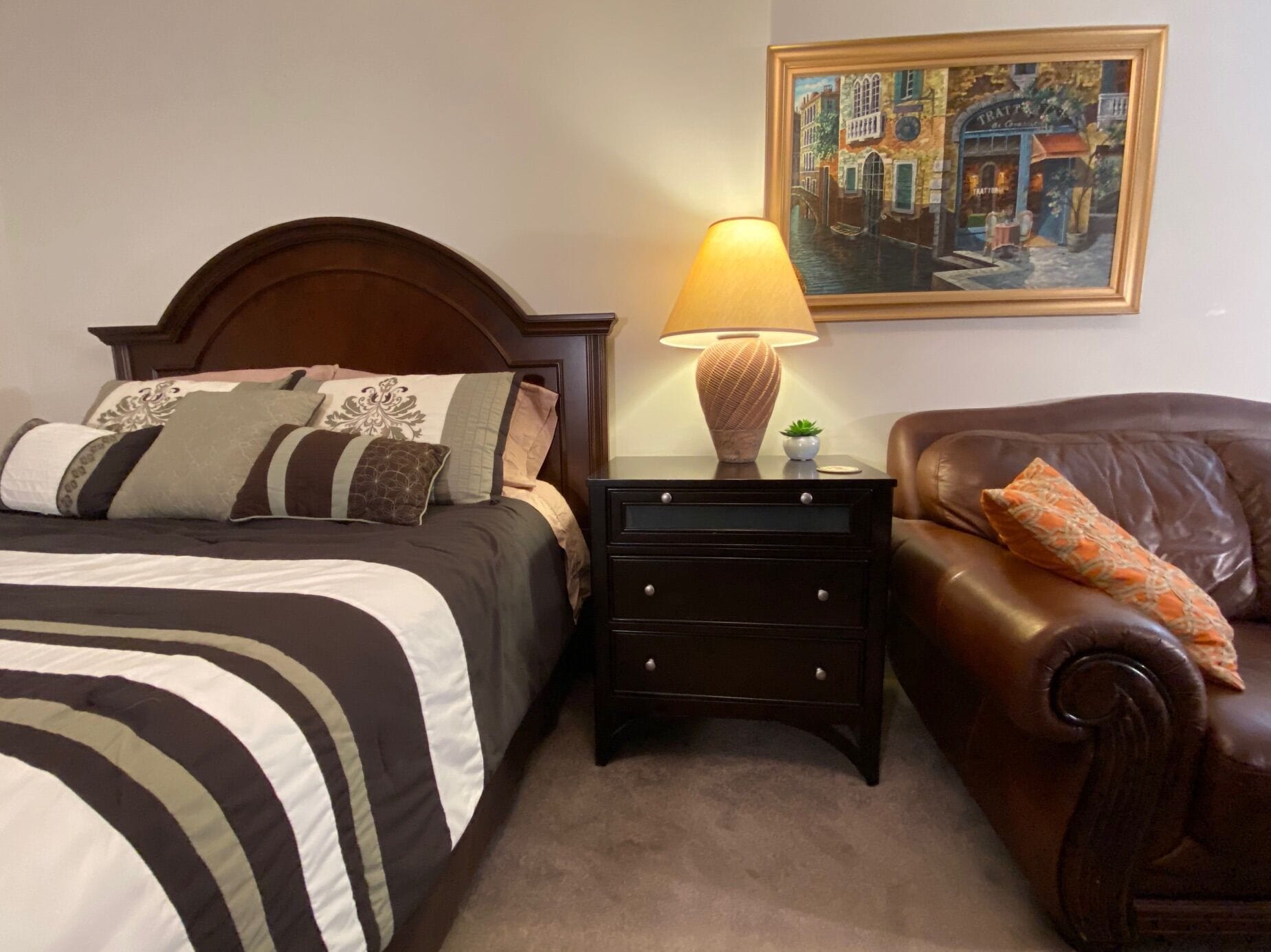 A neatly arranged bedroom with a bed, bedside table, lamp, and a painting on the wall.