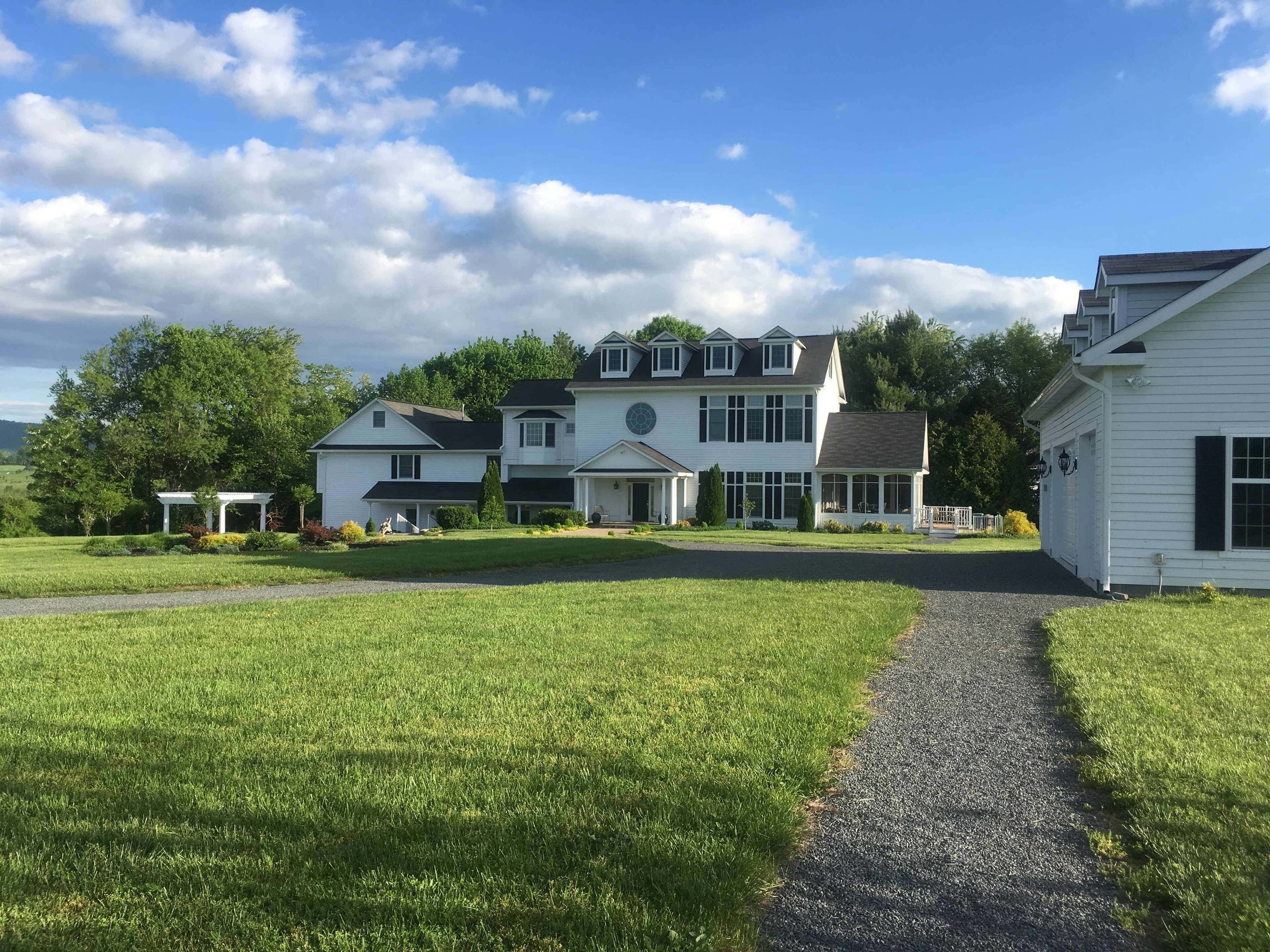 A large, white, two-story house with a covered porch and a driveway leading to the entrance.