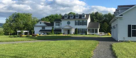 A large, white, two-story house with a covered porch and a driveway leading to the entrance.