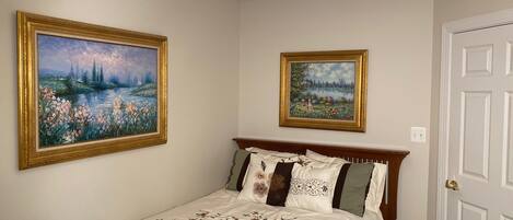 A bedroom with a bed, two framed paintings, a ceiling light, and a door.