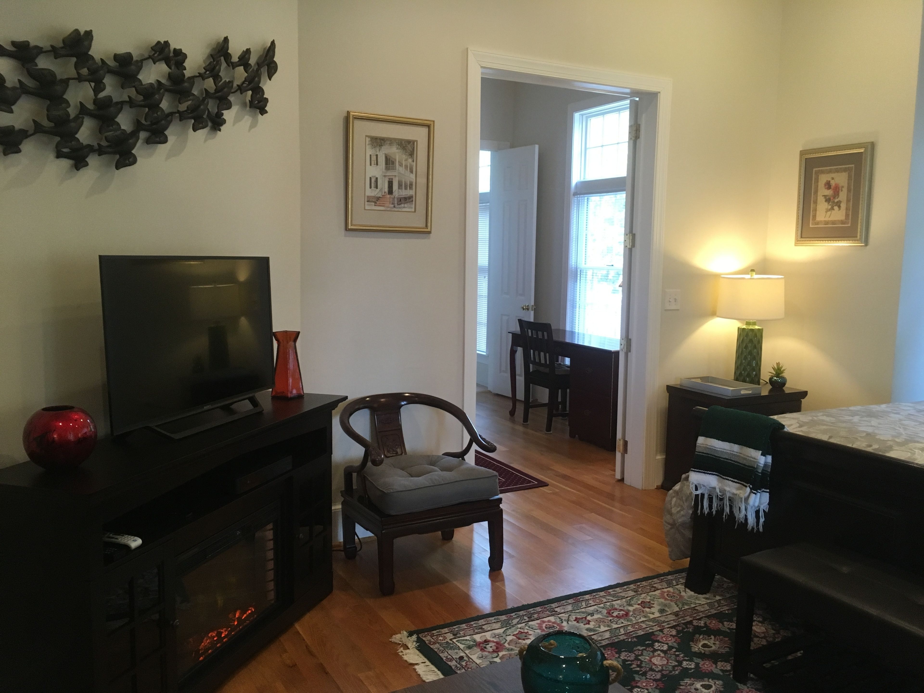 A living room with a fireplace, a television, a dining area with a table and chairs, and a bed with a nightstand.