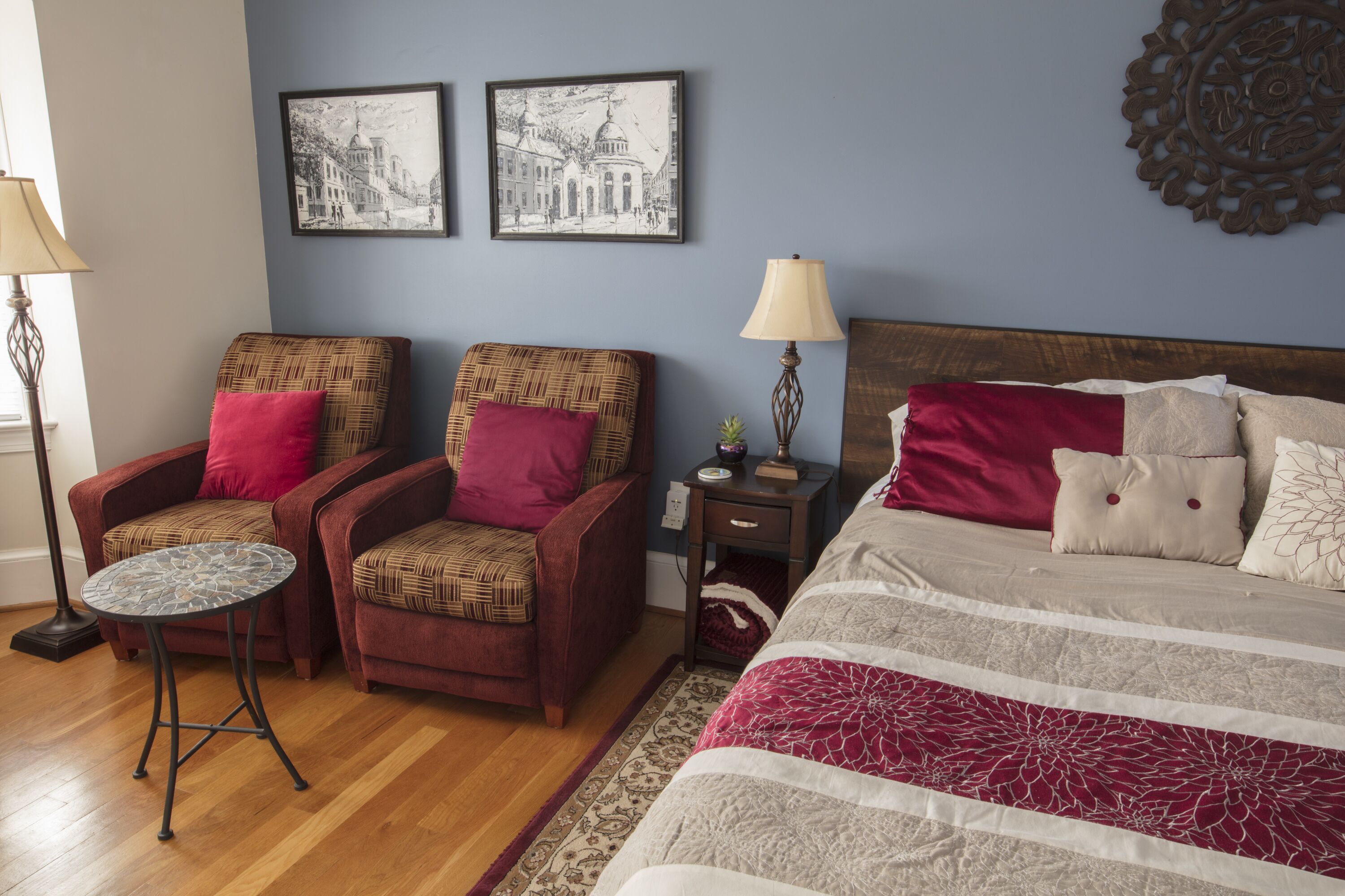 Un dormitorio con cama, dos sillones, una mesita y dos cuadros colgados.