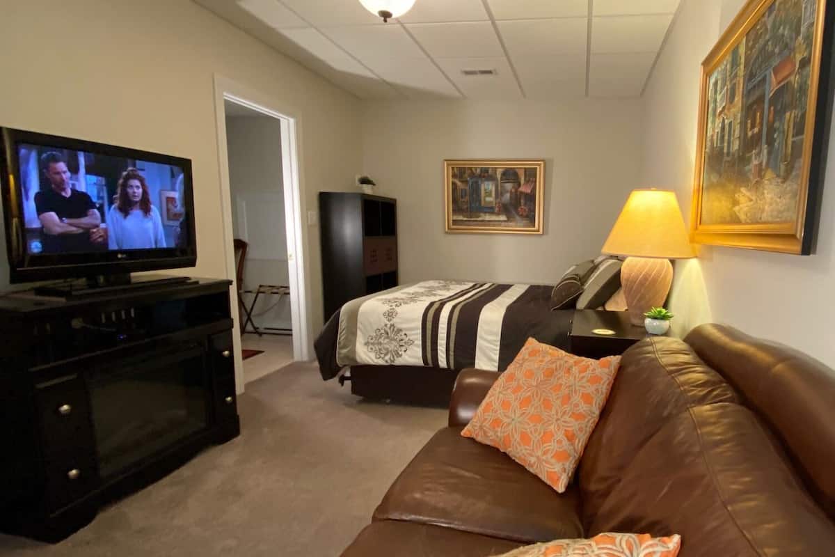 A hotel room with a bed, a brown leather couch, a television, a lamp, and a painting on the wall.