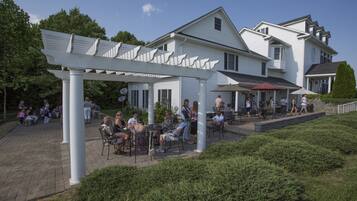 A white building with a covered patio area, outdoor seating, and a small garden.