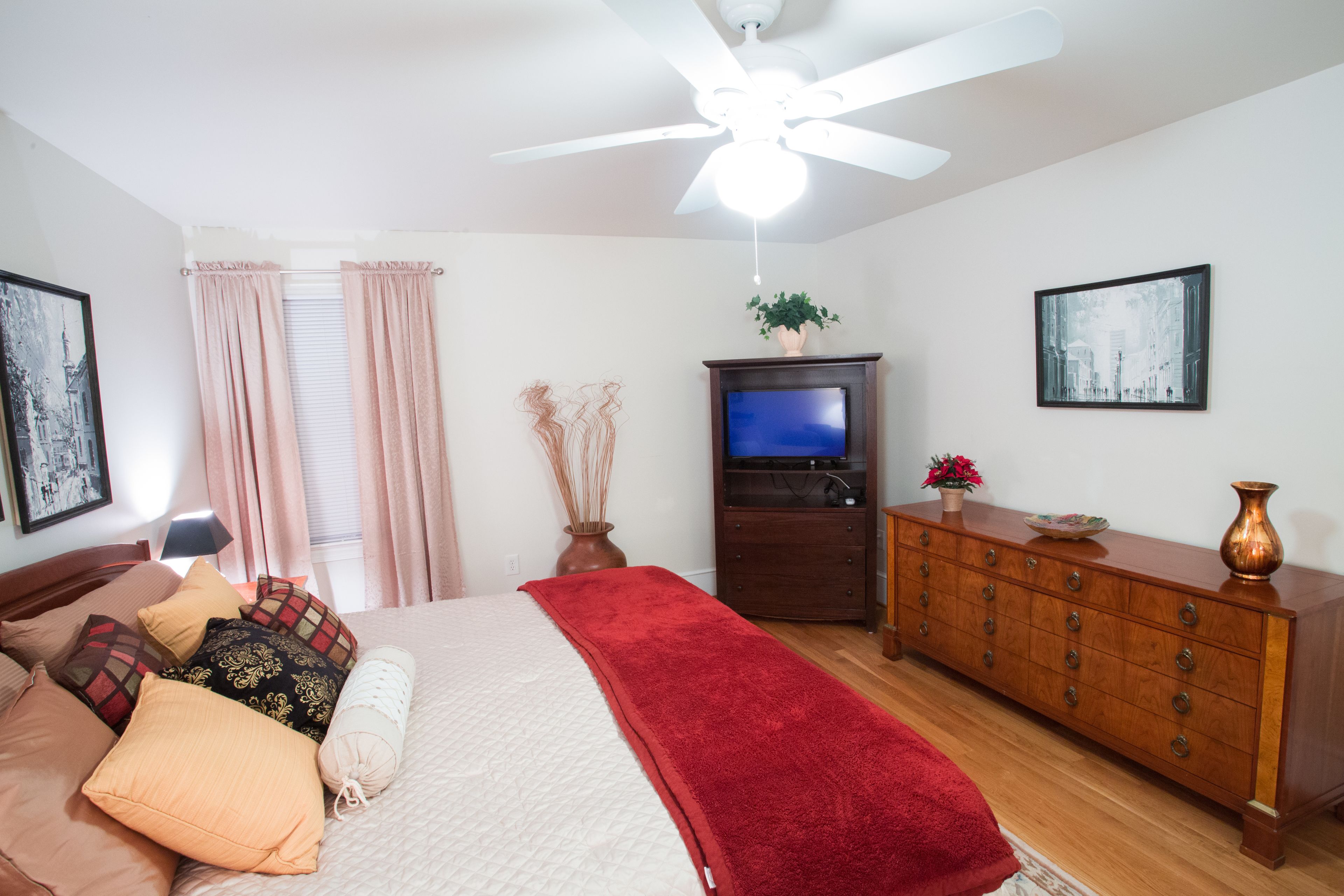 Un dormitorio con una cama, un aparador, un televisor y un ventilador de techo.