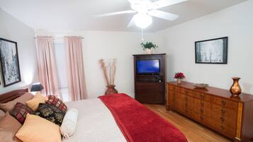 Un dormitorio con una cama, un aparador, un televisor y un ventilador de techo.