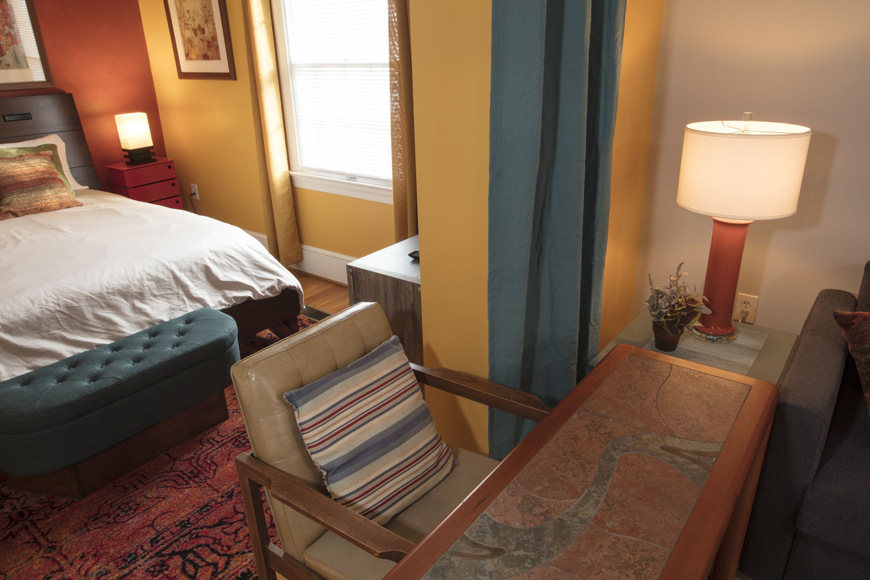 A hotel room with a bed, a chair, a small table, a lamp, and a window with curtains.