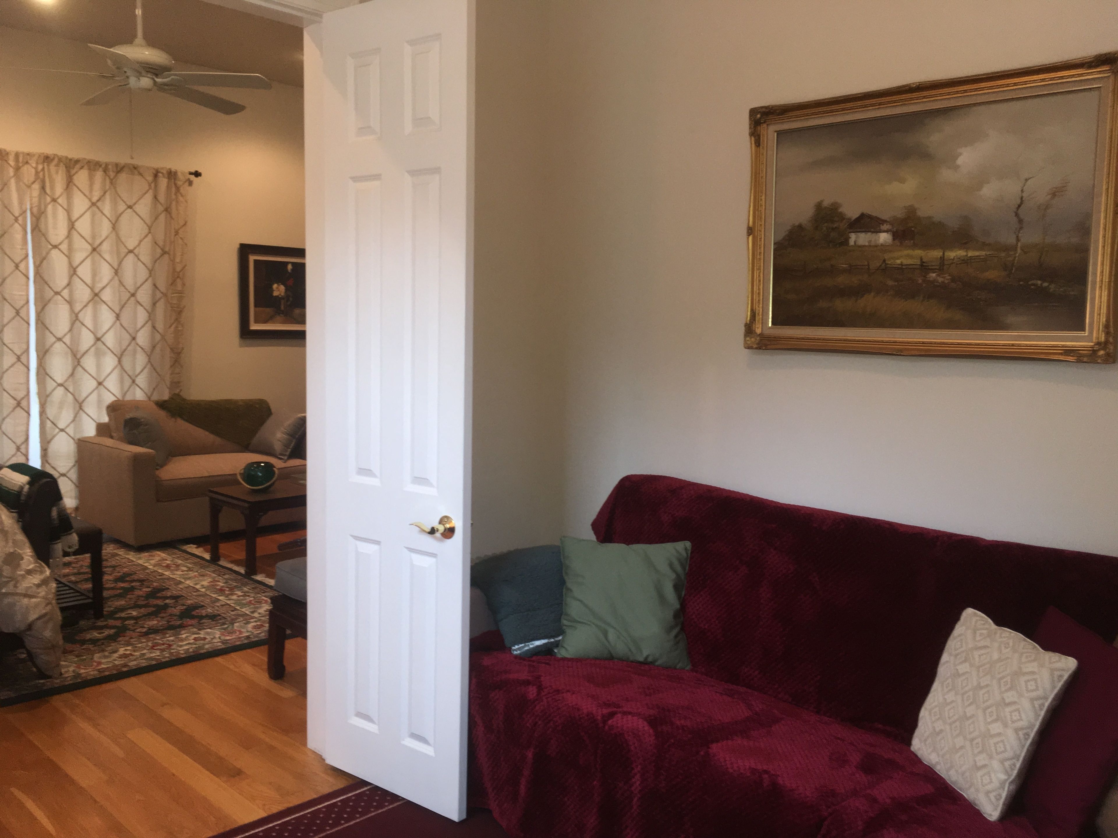 A living room with a red velvet sofa, a white door, a painting on the wall, and a patterned rug.