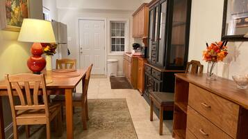 A kitchen with wooden cabinets, a dining table with chairs, a red lamp, and a vase with flowers.