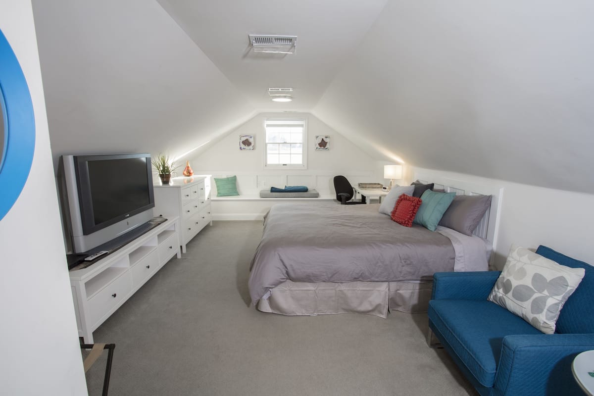 A bedroom with a bed, a TV, a dresser, a blue sofa, and a window.