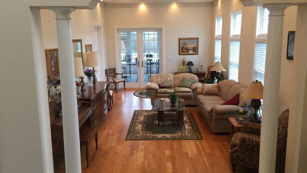 A spacious living room with a wooden floor, a large sofa, a coffee table, and a dining area with a wooden table and chairs.