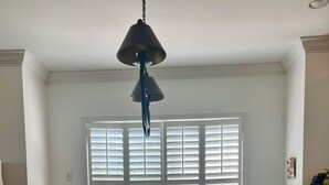 A dining area with a wooden table, white chairs, a hanging light fixture, and a window with blinds. - Great summer rates, Location, Views, Convenience...Golf/Pool/Fitness/Biking (Saint Simons Island)