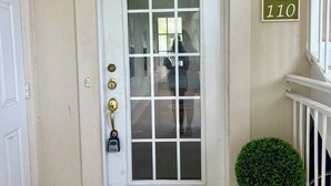 A white door with a glass panel, a brass doorbell, a doormat with "hello" written on it, a small potted plant, and a sign with "WP 110" on the wall. - Great summer rates, Location, Views, Convenience...Golf/Pool/Fitness/Biking (Saint Simons Island)