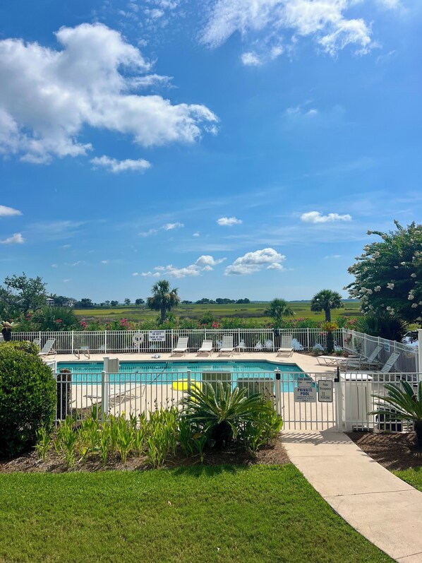 A swimming pool with a white fence, surrounded by greenery and a clear sky.