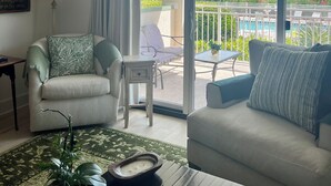 A spacious living room with a large sliding glass door leading to a balcony. The room features a sofa, a chair, a small table, and a decorative plant. - Great summer rates, Location, Views, Convenience...Golf/Pool/Fitness/Biking (Saint Simons Island)
