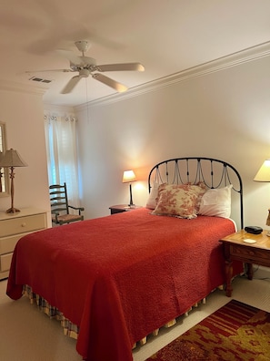 A bedroom with a bed, two bedside tables, a chair, a ceiling fan, and a window with curtains.