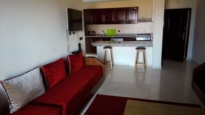 Una sala de estar con un sofá rojo, una zona de cocina con armarios oscuros y un taburete pequeño.