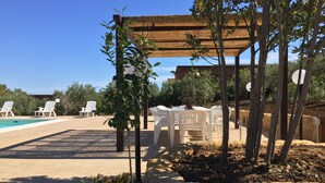 Ein Poolbereich mit weißen Plastikstühlen, einer Holzpergola und einem Tisch mit Sitzgelegenheiten.