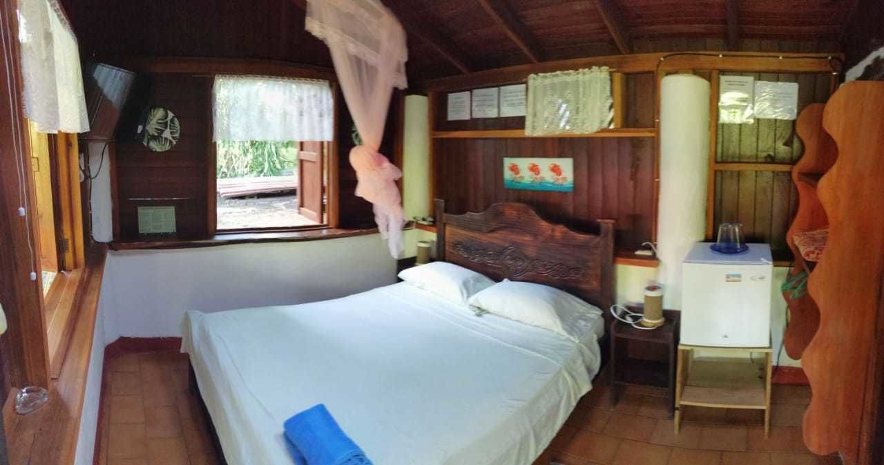 Un dormitorio de cabaña de madera con una cama, un escritorio pequeño, una mesita de noche y una ventana con cortinas.
