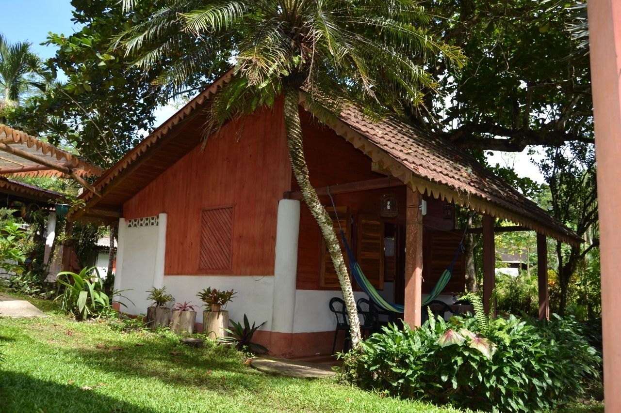 A wooden house with a tiled roof, surrounded by lush greenery and a hammock.
