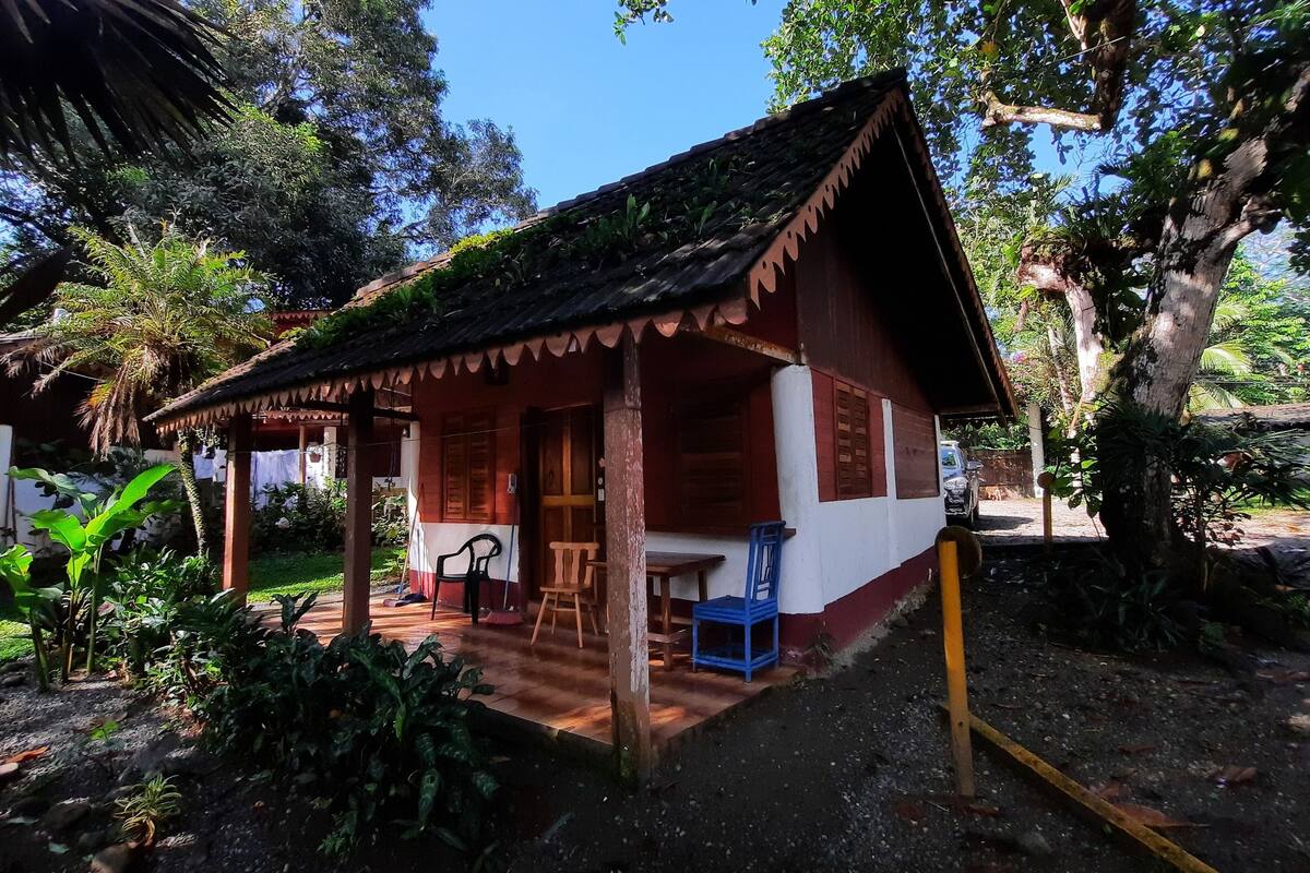 Une petite maison rustique dotée d’un porche, entourée d’une végétation luxuriante.